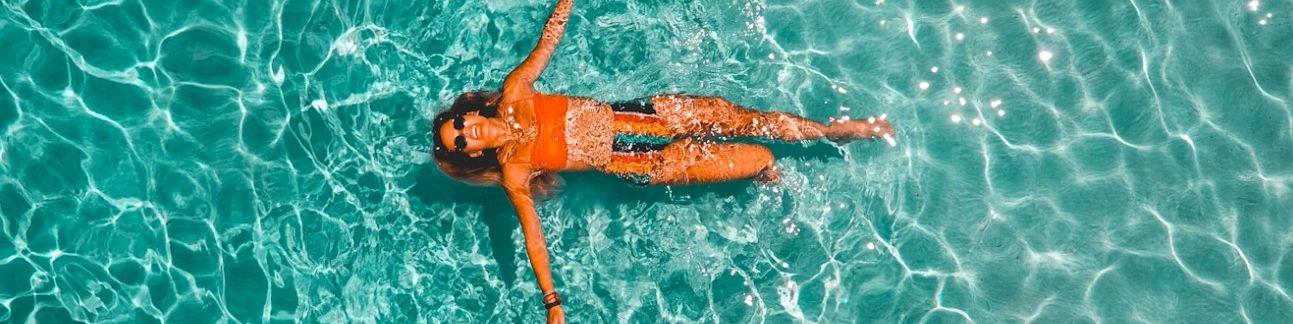 A person floats on clear turquoise ocean water, arms out, viewed from above.
