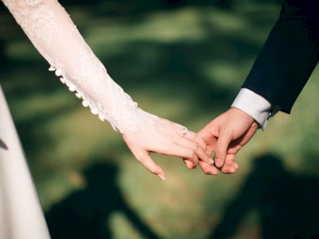 A bride in lace and a groom in a suit hold hands outdoors, symbolizing a wedding bond.