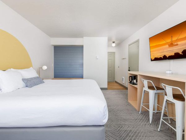 Modern hotel room: white bed, small bar with stools, and a sunset ship picture on the wall.