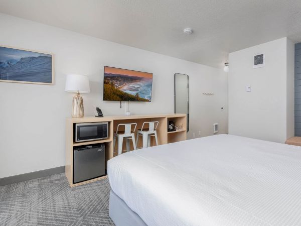 A modern hotel room with a large bed, kitchenette with microwave and fridge, and ocean/mountain wall art.