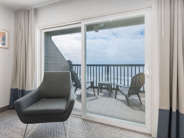 A living room with a large sliding door opening to a balcony with railings, chairs, and overcast sky.