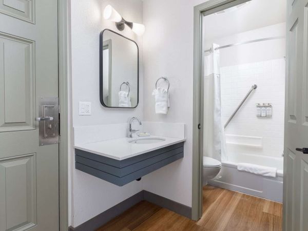 Bright modern bathroom with a dark vanity, wall mirror, and a tub/shower with towels and soap.