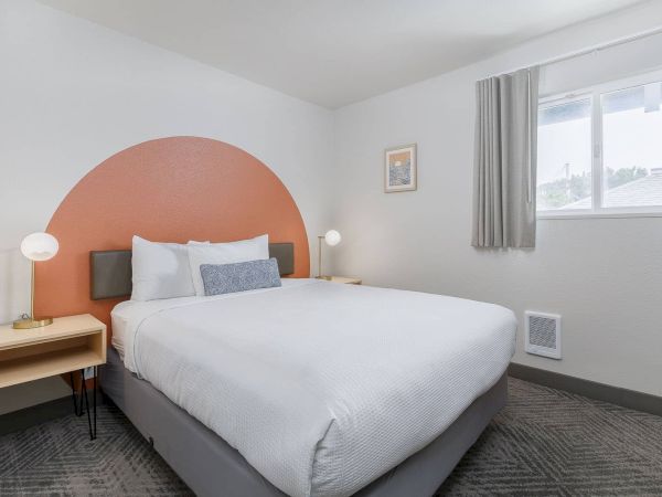 A bright modern bedroom with a large bed, nightstands, and a rounded orange accent wall behind the headboard.