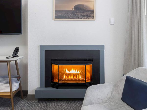 A cozy living room with a lit fireplace, a framed ocean artwork, a small phone by a side table, and a light gray sofa.