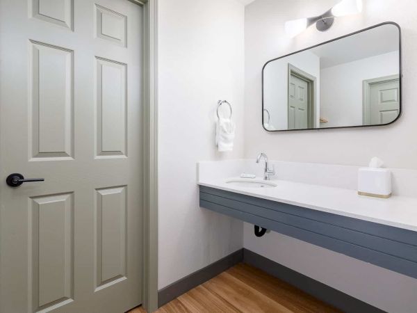 A modern bathroom with a double-sink vanity, black-framed mirror, light fixture, and white doors.