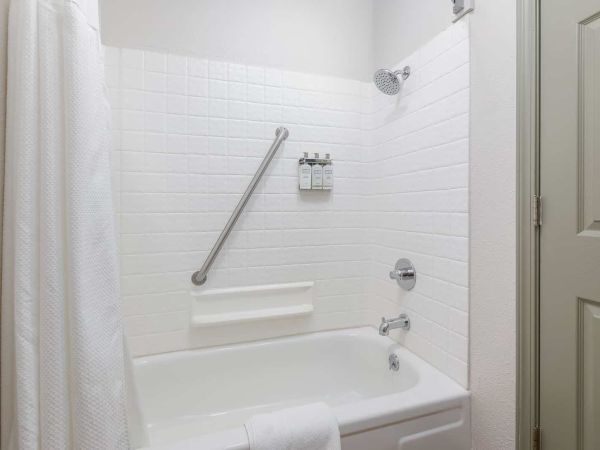 A clean white bathroom with a bathtub, showerhead, curtain, grab bar, and wall soap dispensers.