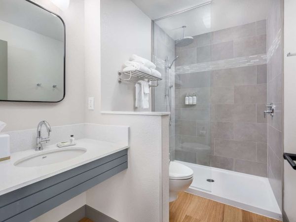 A modern bathroom with a white vanity and sink, a bathtub with glass shower, toilet, and towel racks.