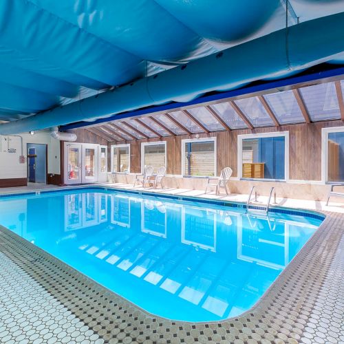 An indoor swimming pool with blue water, tiled deck, and patio doors under a large blue canopy.