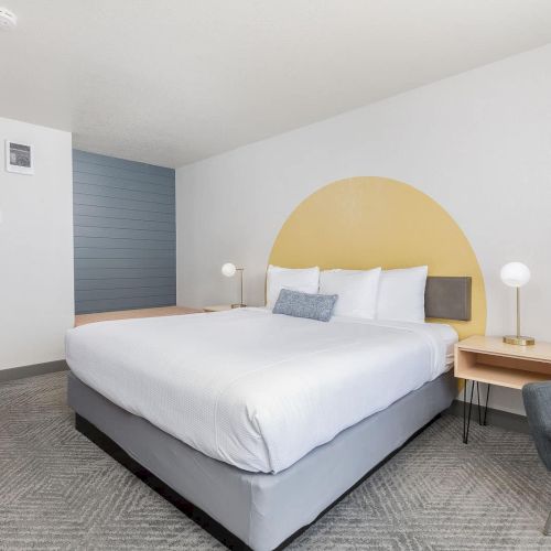 A modern bedroom with a large bed, arched yellow headboard, bedside lamps, and a gray couch.