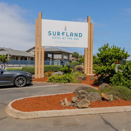 A &ldquo;Surfland Hotel by the Sea&rdquo; sign stands by the roadside outside a hotel, with cars and trees nearby.