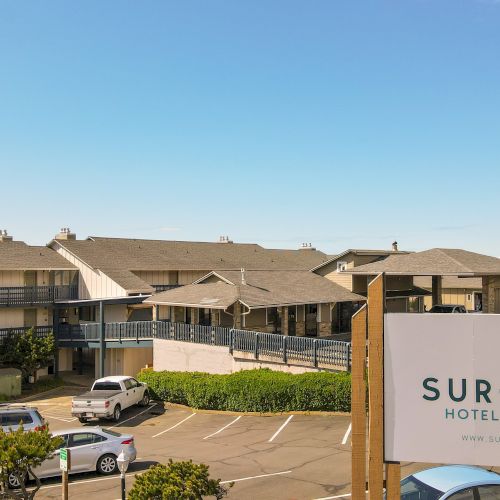 Surfland Hotel by the Sea sign in a parking lot beside low-rise motel buildings under a clear blue sky.