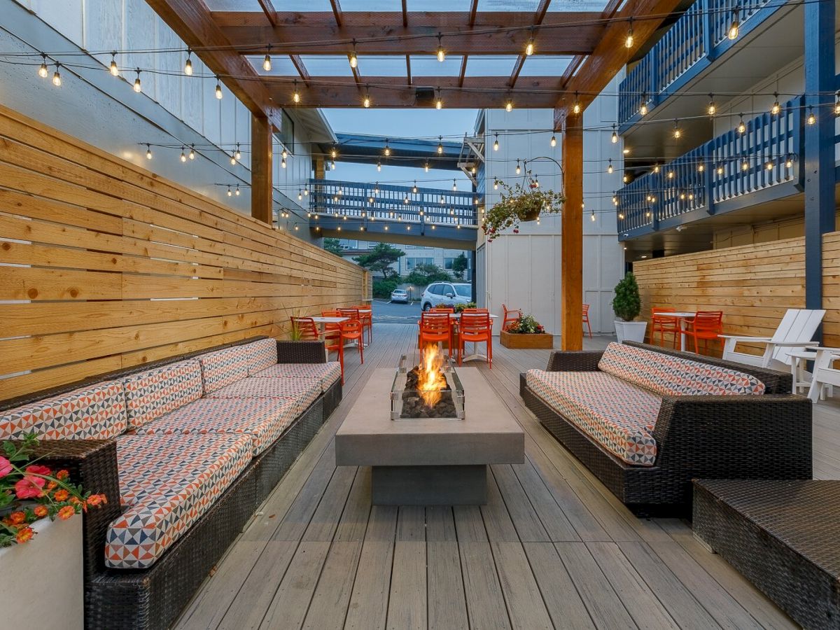 Outdoor patio with string lights, cozy bench seating, and a central gas fire pit, creating a warm gathering spot.